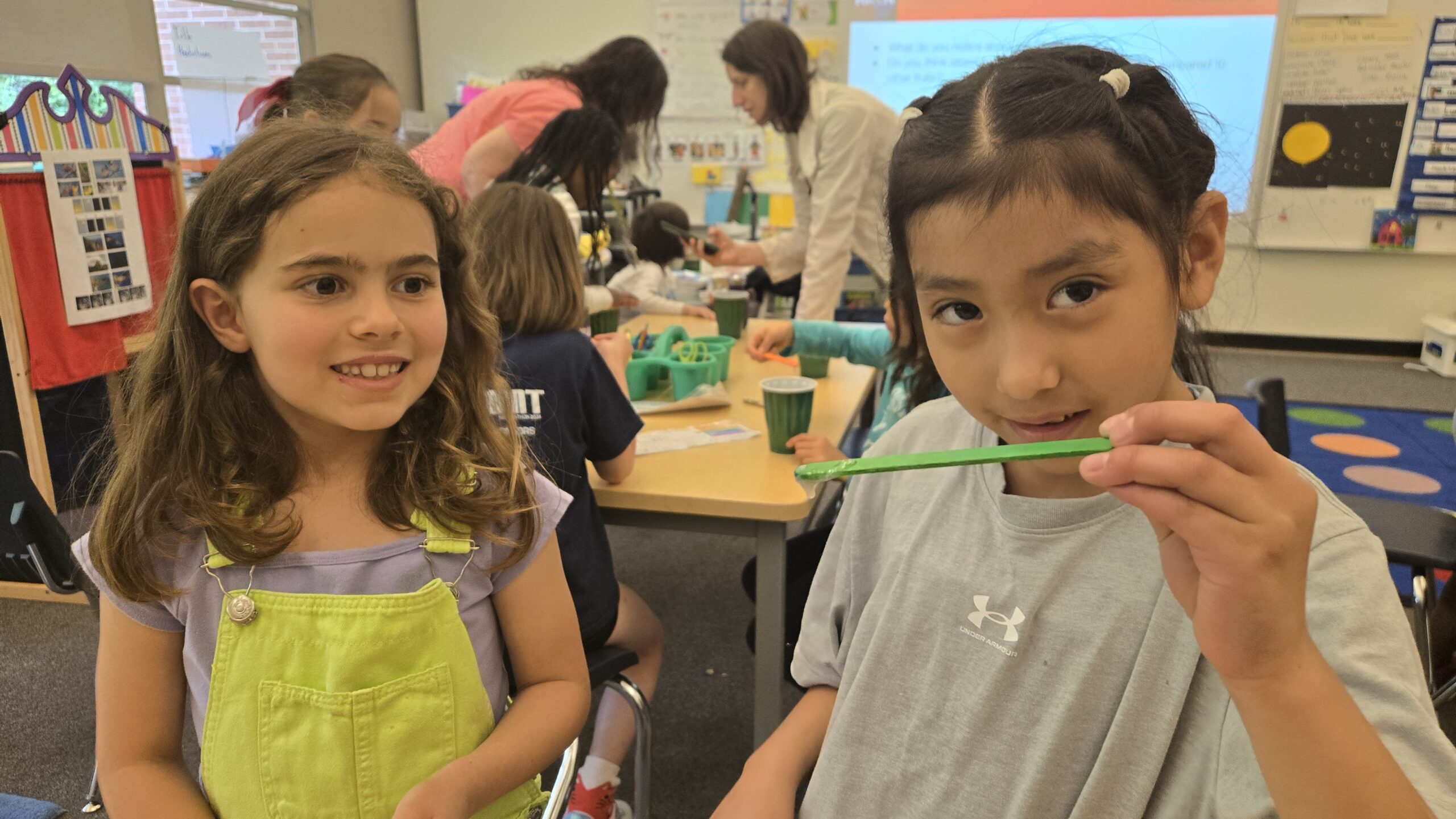 Two girls posing with their science experiment in a classroom.